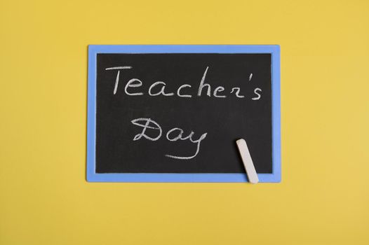 Flat lay of a chalkboard with inscription Teachers Day on a yellow background with space for text