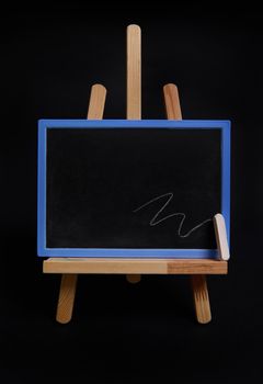 Close-up studio shot of a wooden table easel with a chalk and blackboard with empty blank space for text, isolated on black background with copy space