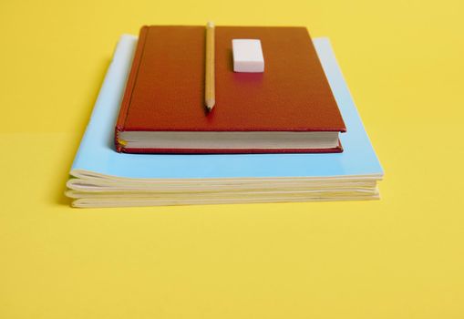 A rubber, pencil on a book with hardcover on textbooks, isolated on yellow background with copy space