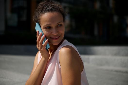 Close-up portrait of a beautiful African American woman talking on mobile phone, looking away, posing to camera on urban high buildings background