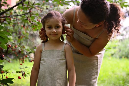 Enjoying time together. Happy family. Positive human emotions. Mom and daughter having a lovely time together during the cherry harvest. Mom puts cherry berry earrings on her daughter's ears.