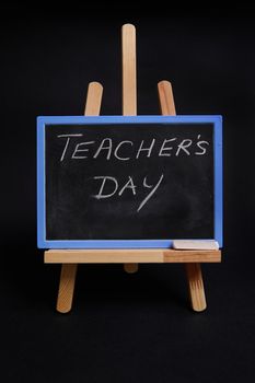 Close-up of a chalk blackboard on a wooden table easel with lettering Teacher's Day , isolated on black background with copy space.