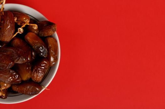 Cropped image of a plate with delicious fresh dates. Red background, copy space. Delicious food to break the fast in Ramadan