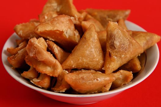 Close-up photography of delicious and sweet plate full of fresh traditional luxurious Moroccan handmade Brewat sweets, isolated on red background.