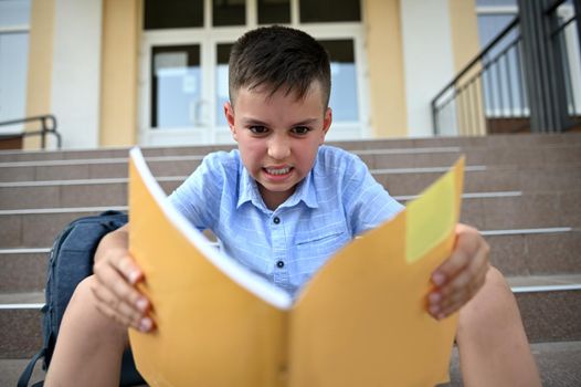 Unhappy, worried, frustrated and angry schoolboy, pupil, feels negative emotions while reading and doing homework. Learning difficulties concept. Back to school