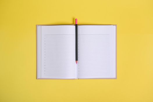 Flat lay composition on yellow background of a color pencil in the middle of an open organizer with clean blank white sheets with copy space.