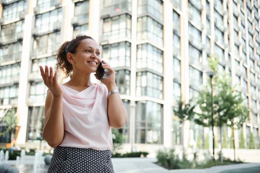 Young mixed race African American woman talking on mobile phone on the background of urban high buildings. Business and communication concepts