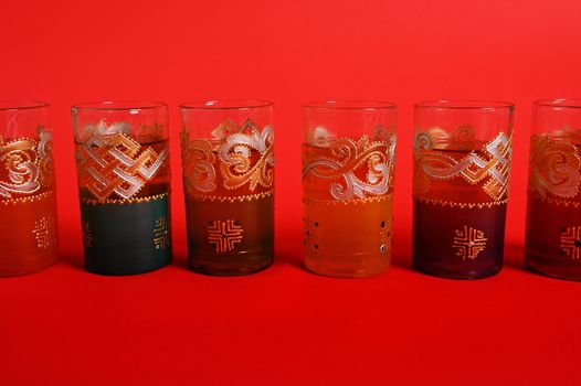 Multicolored glasses for Moroccan green mint tea, decorated in oriental style. Isolated on red background with copy space