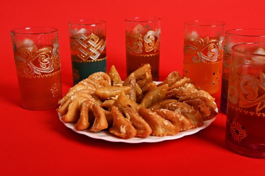 Multicolored glasses of mint tea in Moroccan tradition, with beautiful decoration and a plate with Arabic sweet dessert in the foreground. Isolated on red background. Copy space