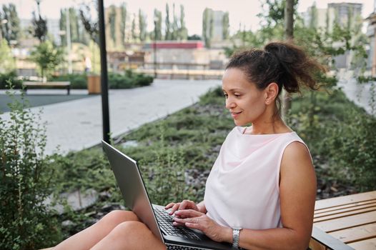 Mature woman working, using laptop sitting on a bench. Freelance work, vacations, distance work, social distancing, e-learning, connection, creative professional, new business, meeting online concept