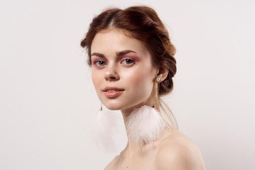 woman with bare shoulders bright makeup fluffy earrings fashion light background. High quality photo