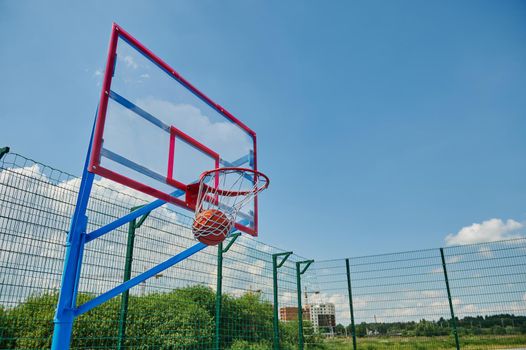A basketball ball in the basket. Scoring a goal on the summer sports court during a basketball game. Basketball through the basket during the match