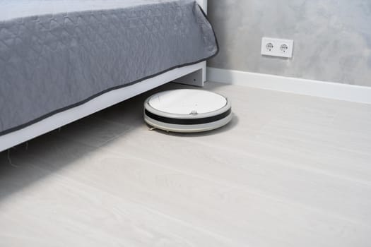 Robotic vacuum cleaner on laminate wood floor in bedroom