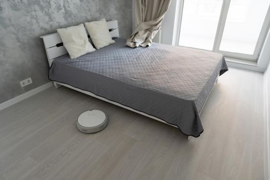 Robotic vacuum cleaner on laminate wood floor in bedroom