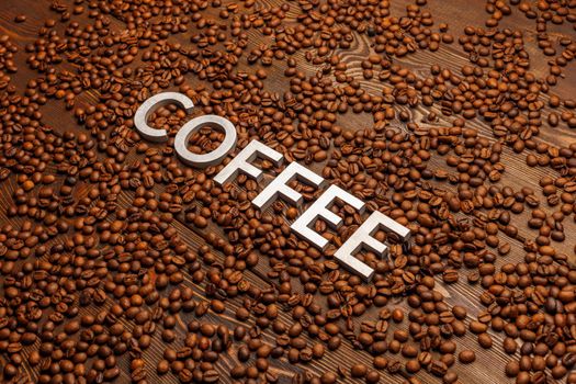 the word coffee laid with silver letters on wooden board surface covered with roasted coffee beans - diagonal perspective full frmae view