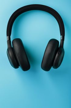 Wireless black headphones on a blue background. View from above. In-ear headphones for playing games and listening to music tracks. Modern style