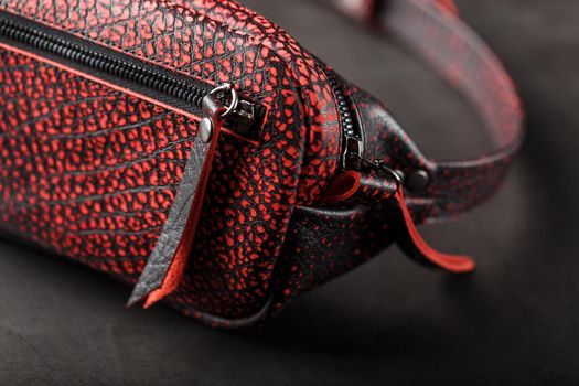 Belt bag made of textured, spotty black and red leather on a stone dark background. Elegant black and red bag with a zipper. Genuine leather, handmade. Banana bag