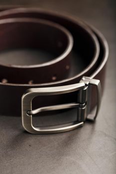 Fashionable men's brown belt made of genuine leather with a light metal buckle on a dark background. Genuine leather, handmade. Close-up