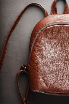 Brown backpack made of textured brown leather on a black stone background. Elegant golden brown women backpack with fashion and rivets. Genuine leather, handmade.