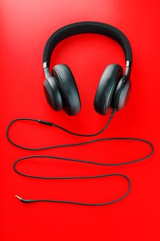 Wireless black headphones on a red background. View from above. In-ear headphones for playing games and listening to music tracks. Modern style