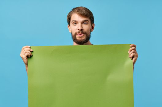 Cheerful man holding green mockup poster discount blue background. High quality photo