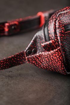 Belt bag made of textured, spotty black and red leather on a stone dark background. Elegant black and red bag with a zipper. Genuine leather, handmade. Banana bag