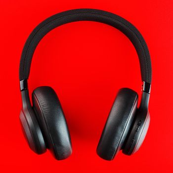 Black wireless headphones on a red background. Overhead, isolated professional-grade headphones for DJs and musicians. View from above.