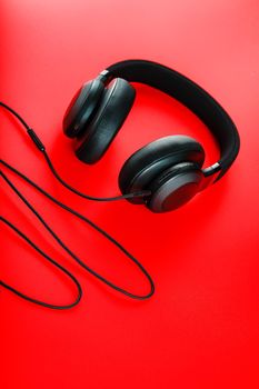 Wireless black headphones on a red background. View from above. In-ear headphones for playing games and listening to music tracks. Modern style