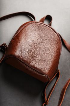 Brown backpack made of textured brown leather on a black stone background. Elegant golden brown women backpack with fashion and rivets. Genuine leather, handmade.