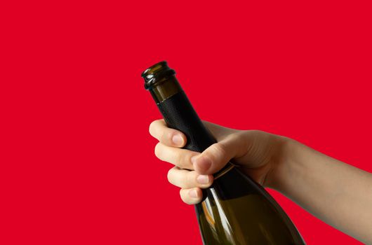 A woman's hand holding an open bottle of champagne on a red background.Holiday concept.