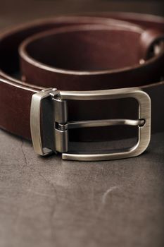 Fashionable men's brown belt made of genuine leather with a light metal buckle on a dark background. Genuine leather, handmade. Close-up