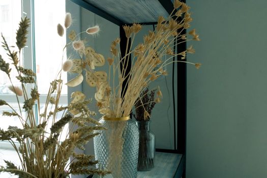 A bouquet of dried flowers in a modern glass vase on a wooden shelf. A place for text, a place to copy