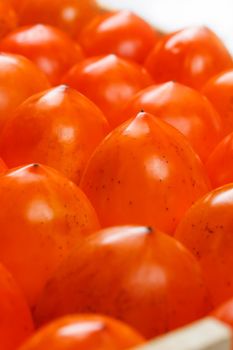 Fresh ripe persimmons in market. Persimmons background. Repeating rows of juicy, ripe persimmon in a box. Close-up, macro