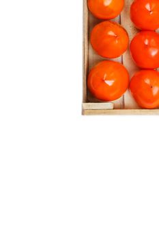 Persimmon fruit in the wooden box isolated on white. Clipping Path included. Juicy ripe persimmon in a large wooden box on a white background. The edge of a wooden box with orange persimmon and a place for text on a white background