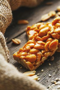 Sweets bar of peanuts on a vintage background with burlap. Delicious oriental sweets Gozinaki from sunflower seeds, sesame and peanuts, covered with honey with a shiny icing. Country style. Macro, vertical frame