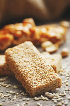 Sweets Bar of sesame on a vintage background with burlap. Delicious oriental sweets Gozinaki from sunflower seeds, sesame and peanuts, covered with honey with a shiny icing. Country style. Macro, vertical frame