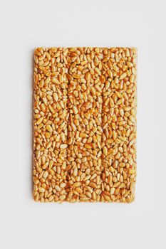 A large golden tile of sunflower seeds, a bar in a sweet molasses on a white background. Kozinaki useful and tasty sweets of the East. Top view, isolated.