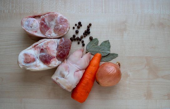 Raw pork meat and leg, carrots and onions on the kitchen table for making jelly.