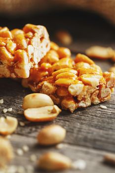 Sweets bar of peanuts on a vintage background with burlap. Delicious oriental sweets Gozinaki from sunflower seeds, sesame and peanuts, covered with honey with a shiny icing. Country style. Macro, vertical frame