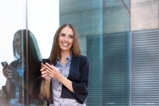 Business woman 35 years dressed stripe shirt black jacket with long hair standing near office building outdoor hold smartphone in hand Happy Caucasian female business person use technology