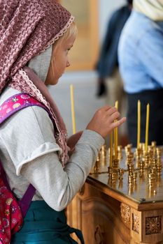 A young parishioner lights a candle at the altar in the church. Believer girl with candles in the church