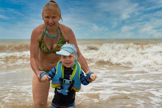 A woman takes a child in a life jacket out of the stormy sea. Vacation safety at sea