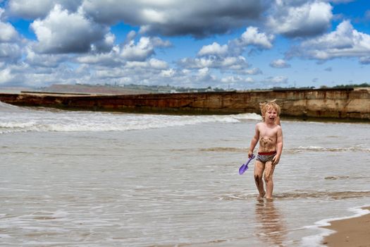 A little boy runs along the sandy beach along the seashore. Child resting on the sea