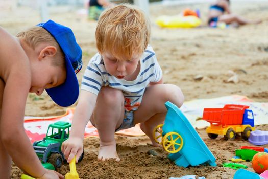 Two children play in the sand with plastic toys. Children playing in the sandbox