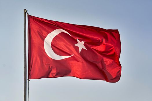 Turkish flag waving in the wind against the background of the sky. White crescent moon and star on red turkish flag