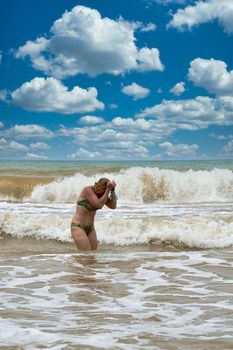 A woman in a swimsuit with white long hair comes out of the sea. Bathing blonde at the sea in summer