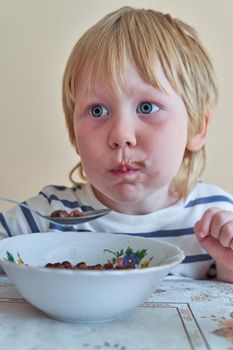 Little boy is having breakfast with chocolate balls with milk. Child eats dry breakfast with milk