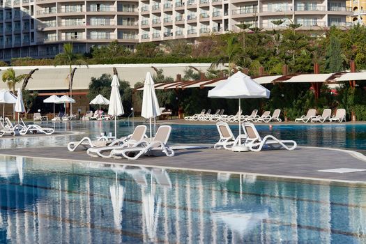 Pool with blue water, sun loungers and parasols in the background of the hotel. Place of rest for tourists at the hotel