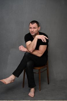 a man sits on a chair, looking to the side with a displeased emotion on a gray background