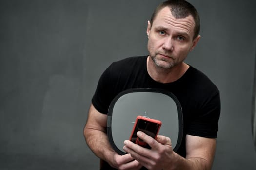 man holding a smartphone in his hands and looking directly at the camera on a gray background